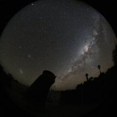 The Milky Way in the night sky. A silhouette of a telescope is visible in the foreground.