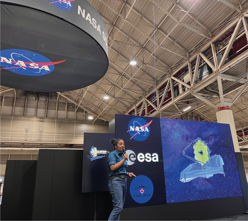 NASA researcher for JWST speaking at a NASA event in front of a screen with the JWST. 