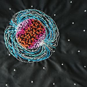 A neutron star recreated using shades of red, pink and blue beads and threads.