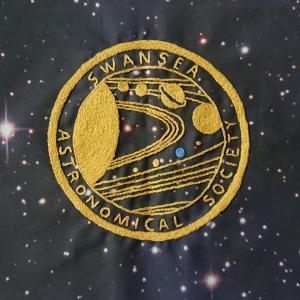 The badge of the Swansea Astronomical Society in yellow embroidery on a star filled background.