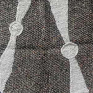 The square shows two pulsars, knitted in white wool on a grey wool background. Pulsars are spinning neutron stars that emit radio light in beams, which makes a lighthouse like effect (the pulsars are shown by the circles and the beams by the wedges coming from them). 