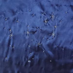 Stars of the Pleiades constellation embroidered in silver thread on a blue background.