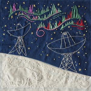 European Incoherent Scatter Radars on Svalbard embroidered in white thread on a blue background. Above them the northern lights are embroidered in red and green threads. In the bottom left corner a polar bear is embroidered in white thread.