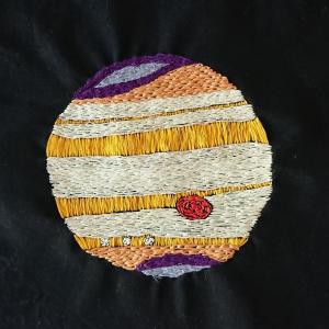 Jupiter in the optical waveband with its X-ray aurorae superimposed at the poles. Embroidered in white, yellow, orange and purple threads on a black background.