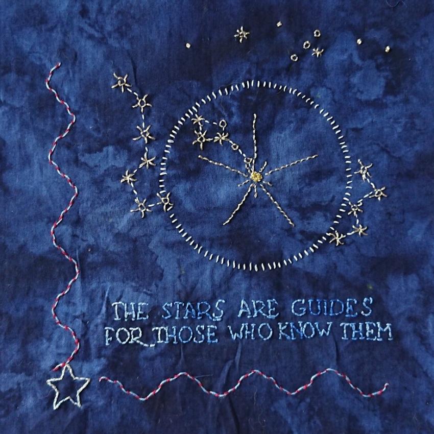 Embroidered constellations and asterisms, a compass and a quote "The Stars are Guides for Those Who Know Them" on a blue background.