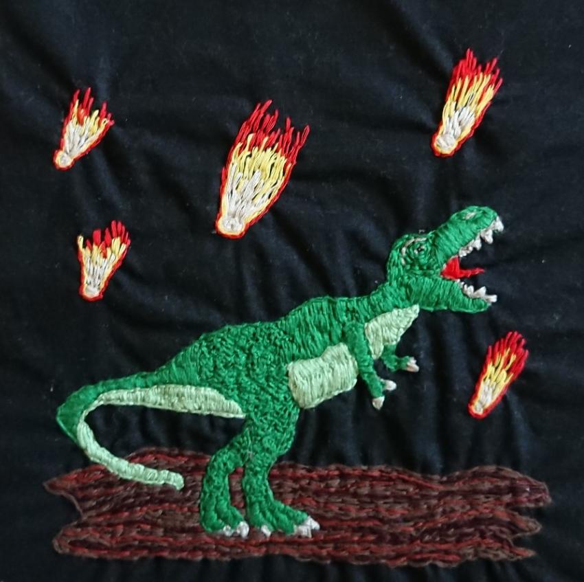 Embroidered T-rex with asteroids coming down from the sky.