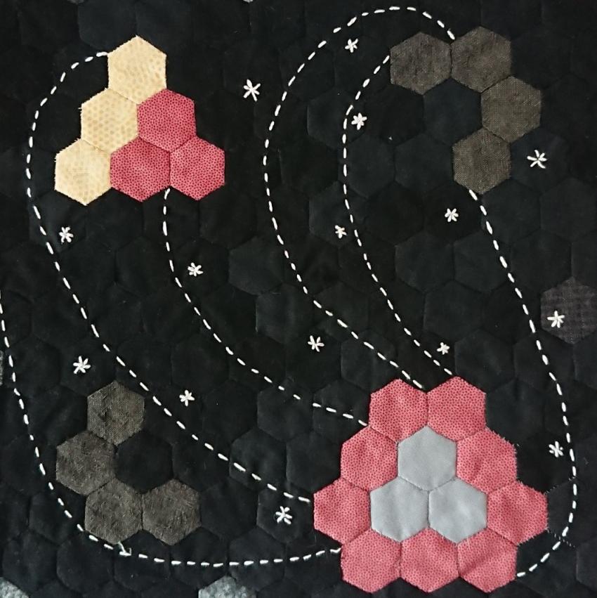 Black, grey, red and yellow hexagons sewn together to create an abstract image.
