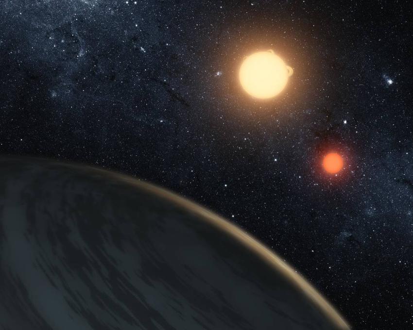 An artist's impression of the circumbinary planetary system Kepler 16-b. A planet is seen in the foreground, with 2 orange and yellow-hued stars in the background. Faint stars can be seen in the background.