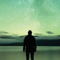 A silhouette of a skygazer against a green-hued night sky, with the Milky Way visible.