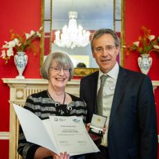 Ambassador Miguel Berger and Professor Gillian Wright stand side by side. Prof. Wright is holding a small box containing the medal and a certificate.