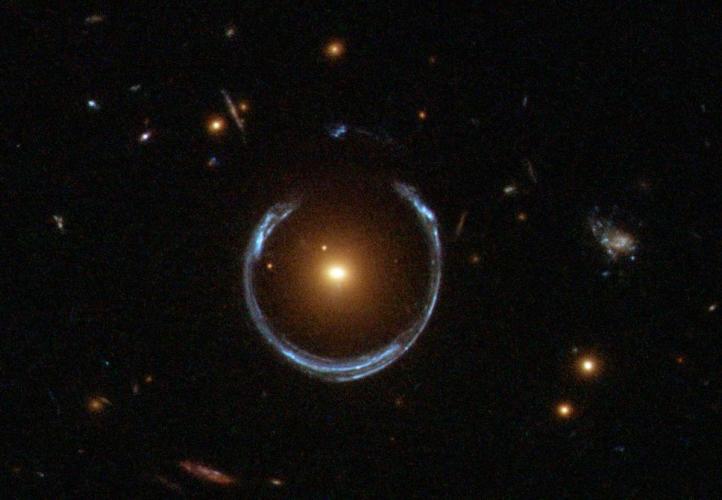 The newly discovered ultramassive blackhole lies at the centre of the orange galaxy. Far behind it is a blue galaxy that is being warped into the horseshoe shaped ring by distortions in spacetime created by the immense mass of the foreground orange galaxy.