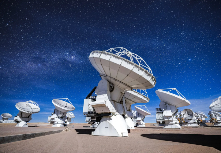 ALMA's DV-59 antenna in the foreground with multiple other antennas observing the sky in a night dominated by the Moon.