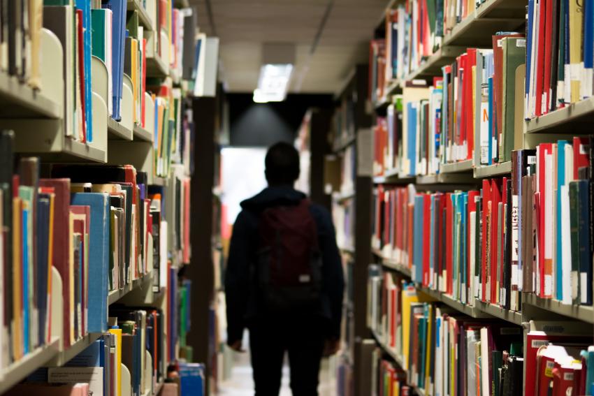 A person walking along aisle in library with shelves full on books on either side