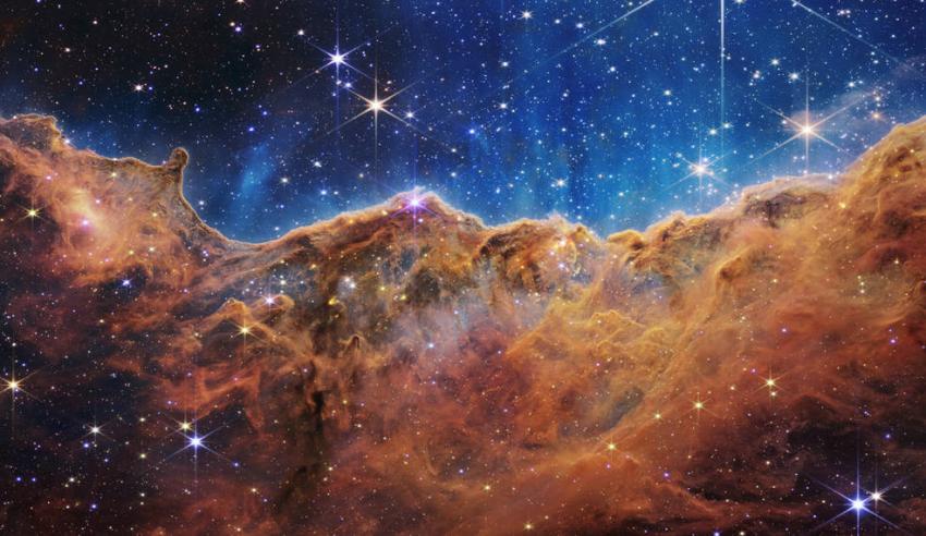 Orange hued nebulous clouds of dust and gas against a blue starry backdrop.